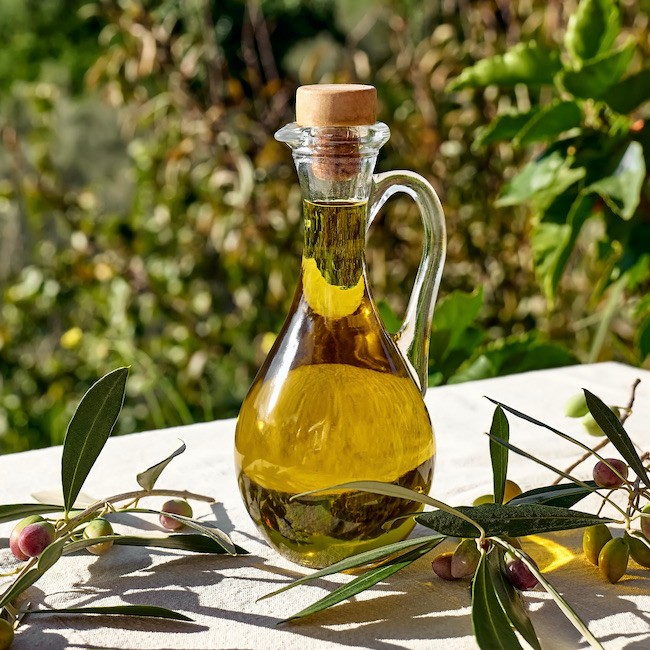 Extra virgin olive oil and olive branch in the bottle on the table with linen tablecloth in the olive grove. Healthy mediterranean food.