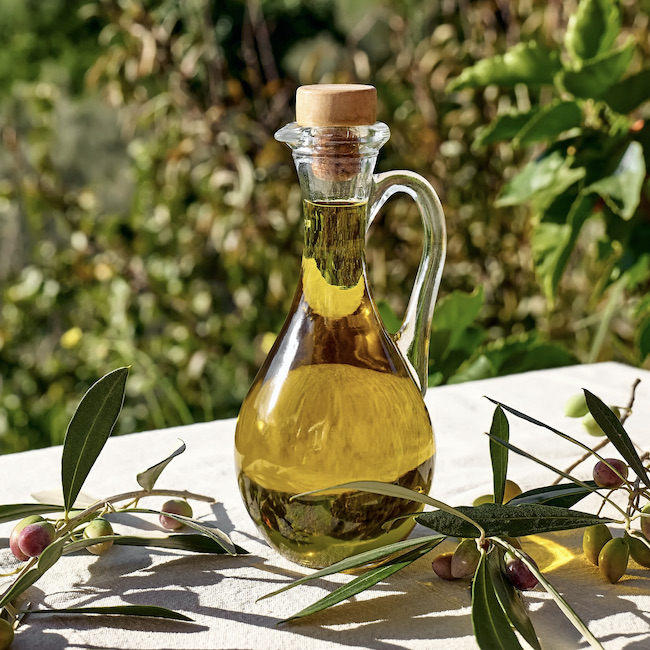 Extra virgin olive oil and olive branch in the bottle on the table with linen tablecloth in the olive grove. Healthy mediterranean food.