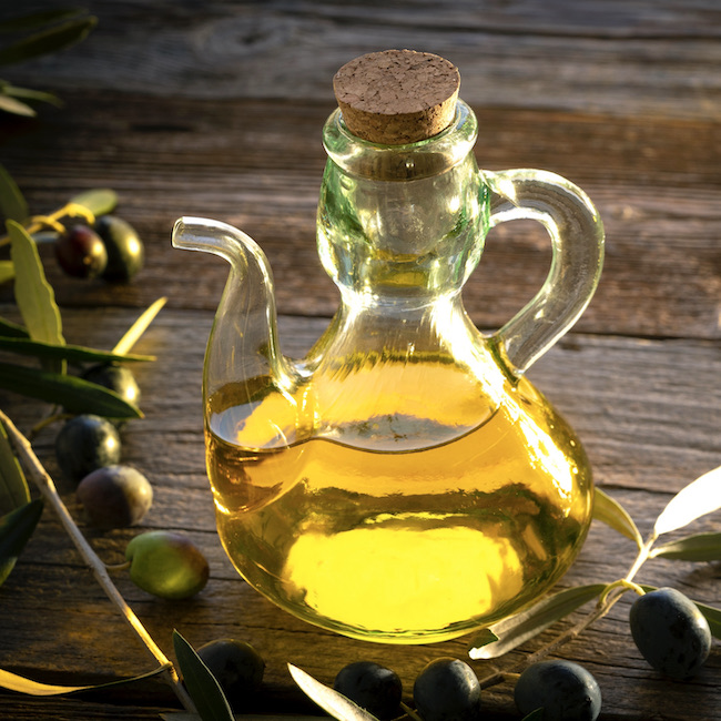 Olive oil bottles with olive tree branches leaves and olives on wooden rustic background at Mediterranean