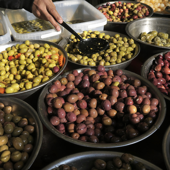 shop owner preparing a sale of olives to a customer at his stall at the Latin Quarter farmer's market, Paris, France