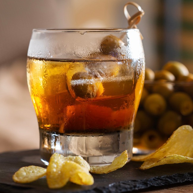 Spanish appetizer with red vermouth, olives, fried potatoes or chips on a table at home. Refreshing and relaxing drink after work