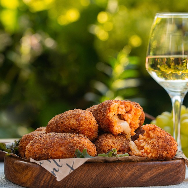 Italian summer aperitif. White wine glasses and snacks: Supplì - italian deep-fried snacks consisting of rise filled with mozzarella, black olives.