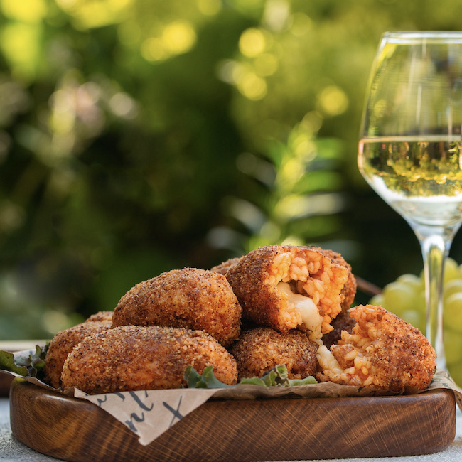 Italian summer aperitif. White wine glasses and snacks: Supplì - italian deep-fried snacks consisting of rise filled with mozzarella, black olives.