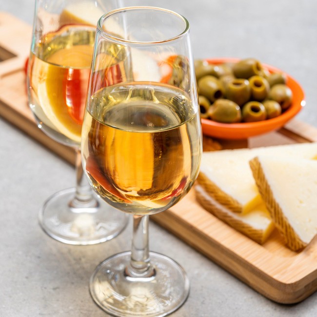 Glasses of dry cold fino sherry wine served with spanish tapas, manchego cheese, green olives, cheese crackers