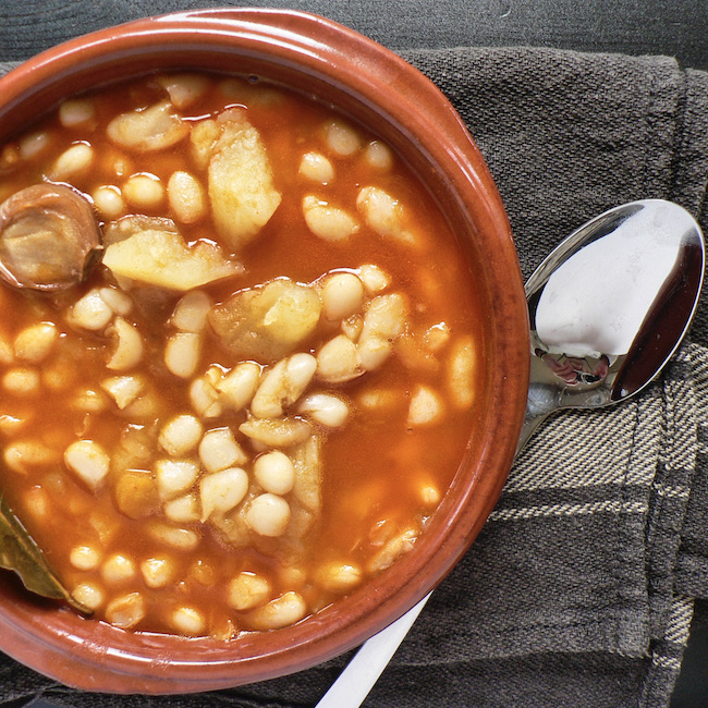 Spanish Asturian fabada in a white plate, spoon on wooden table