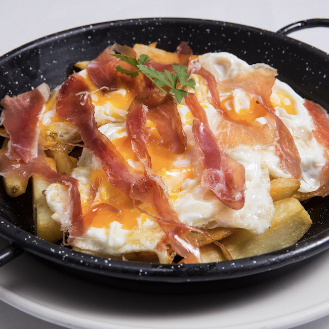 Traditional spanish fried eggs with Jabugo ham served on frying pan