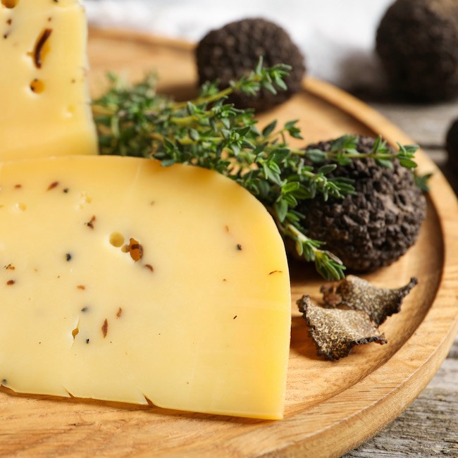 Delicious cheese, fresh black truffles and thyme on wooden plate, closeup