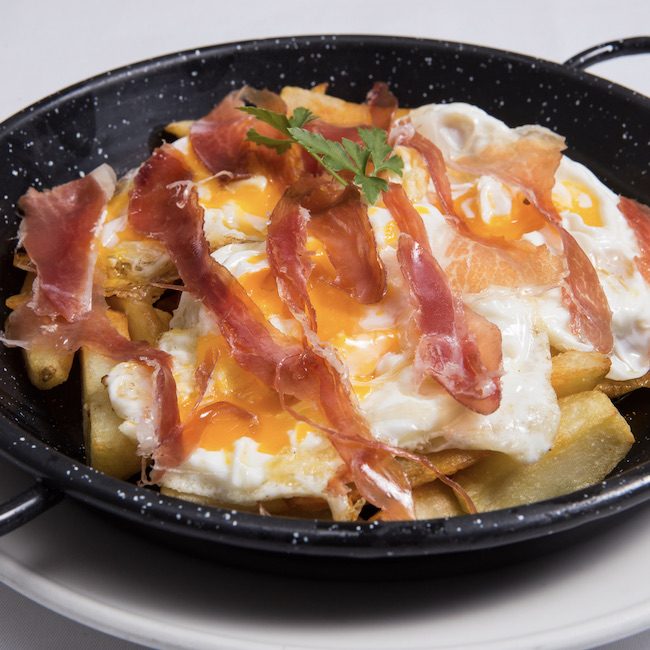 Traditional spanish fried eggs with Jabugo ham served on frying pan