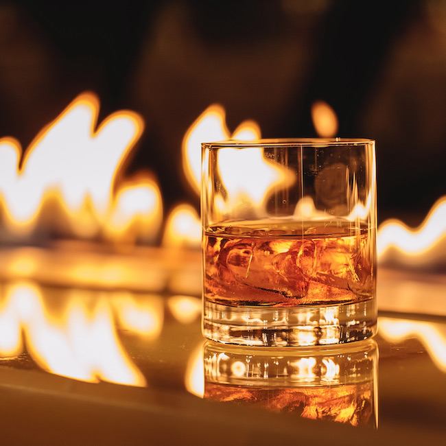 side view of glass of whiskey with ice on a background of a burning flame