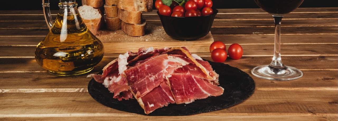 delicious plate of Iberian ham accompanied by tomatoes, olive oil, bread and a glass of wine with a black background on a wooden table