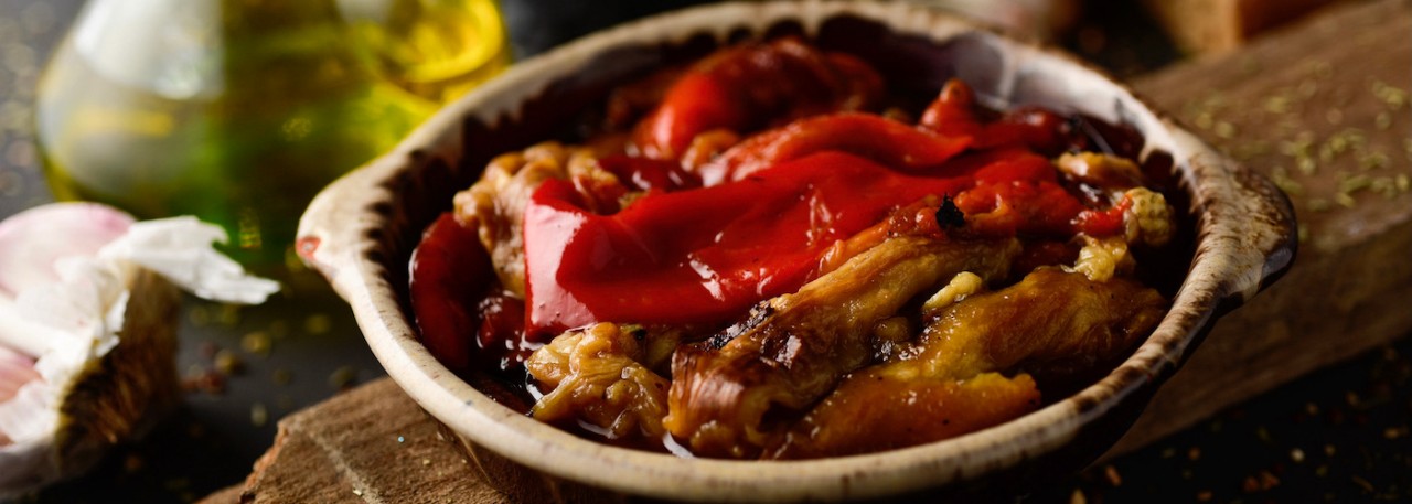 a plate with escalivada, a typical dish of Catalonia, Spain, made with grilled and peeled eggplant, red pepper and onion, on a rustic wooden table next to a cruet with olive oil