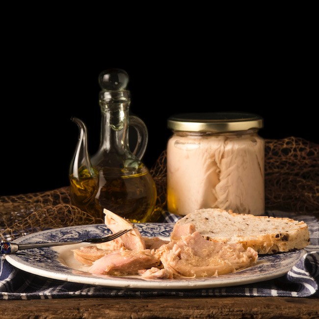 Northern albacore in olive oil, preserved in olive oil on a plate and glass jar on black background