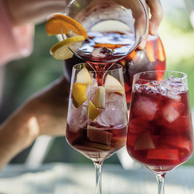 During a photo shoot, a senior woman is pouring some Sangria in wine glasses.