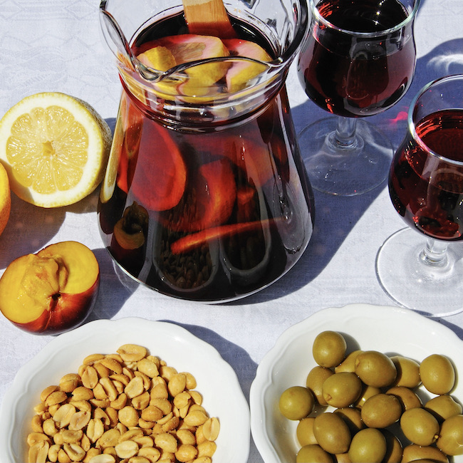A jug of Sangria with a plate of Olives and Salted peanuts.